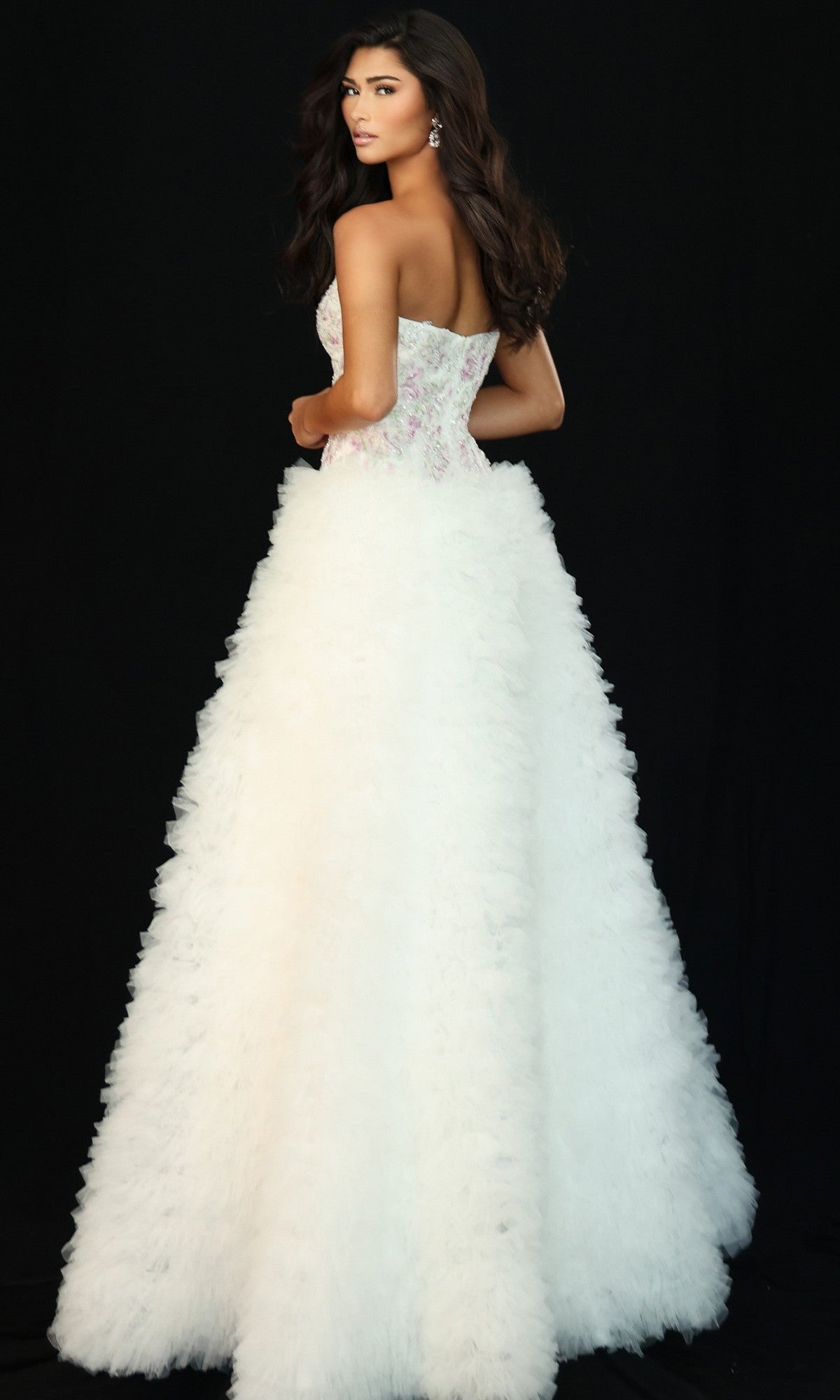 A woman wearing the Jovani 45636 long prom dress, featuring a strapless white bodice and a voluminous textured A-line skirt, stands against a plain black background, looking over her shoulder.
